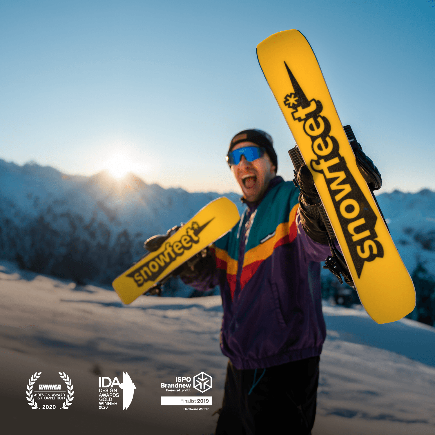 Person holding two yellow short skis with 'snowfeet' branding against a mountainous background.