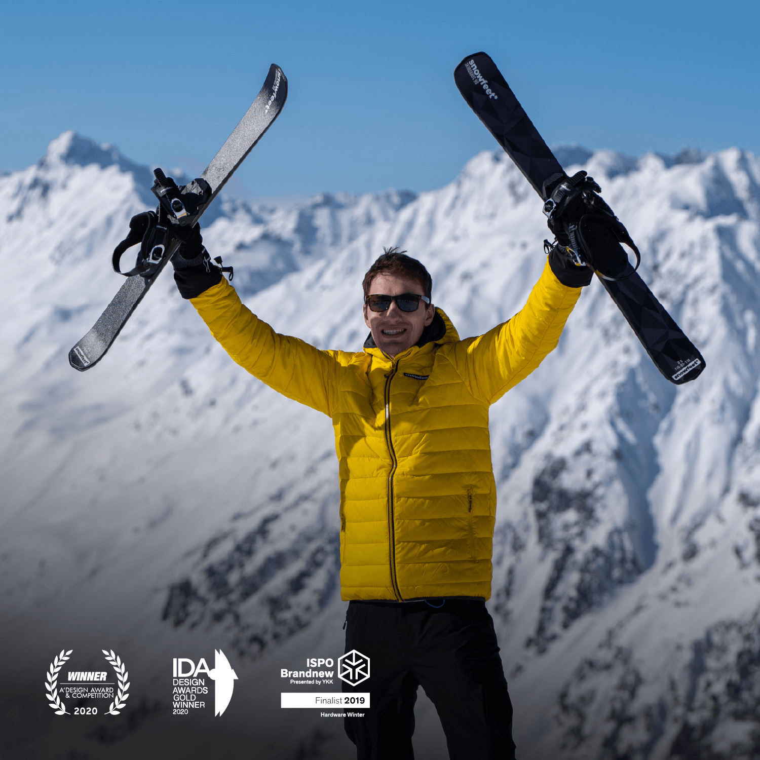 Person in a yellow jacket holding short skis with snowboard binding against a snowy mountain backdrop