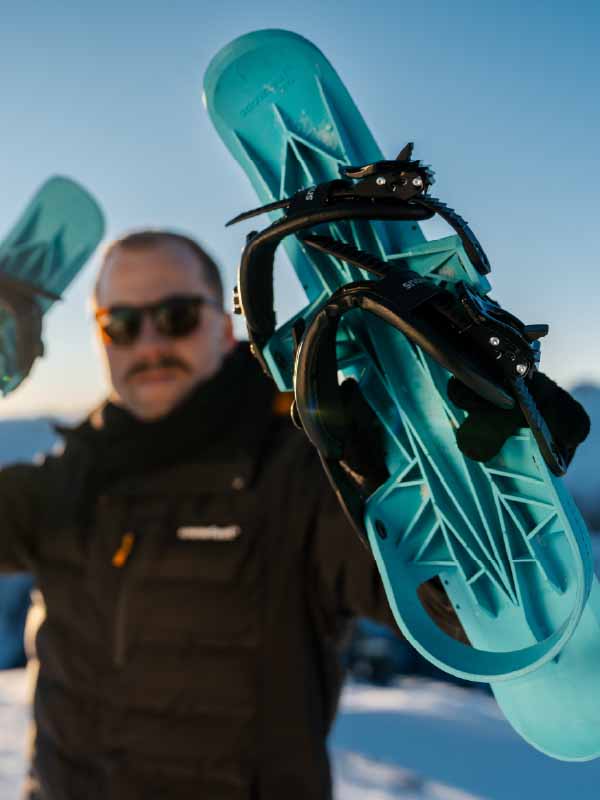 Person holding a teal snowboard with a blurred background